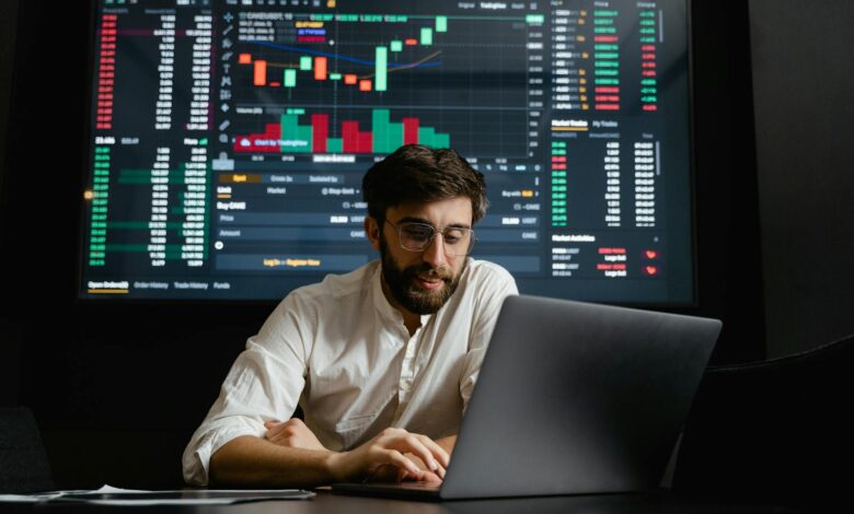 Male analyst studies cryptocurrency trends at a workstation with multiple displays showing market data.